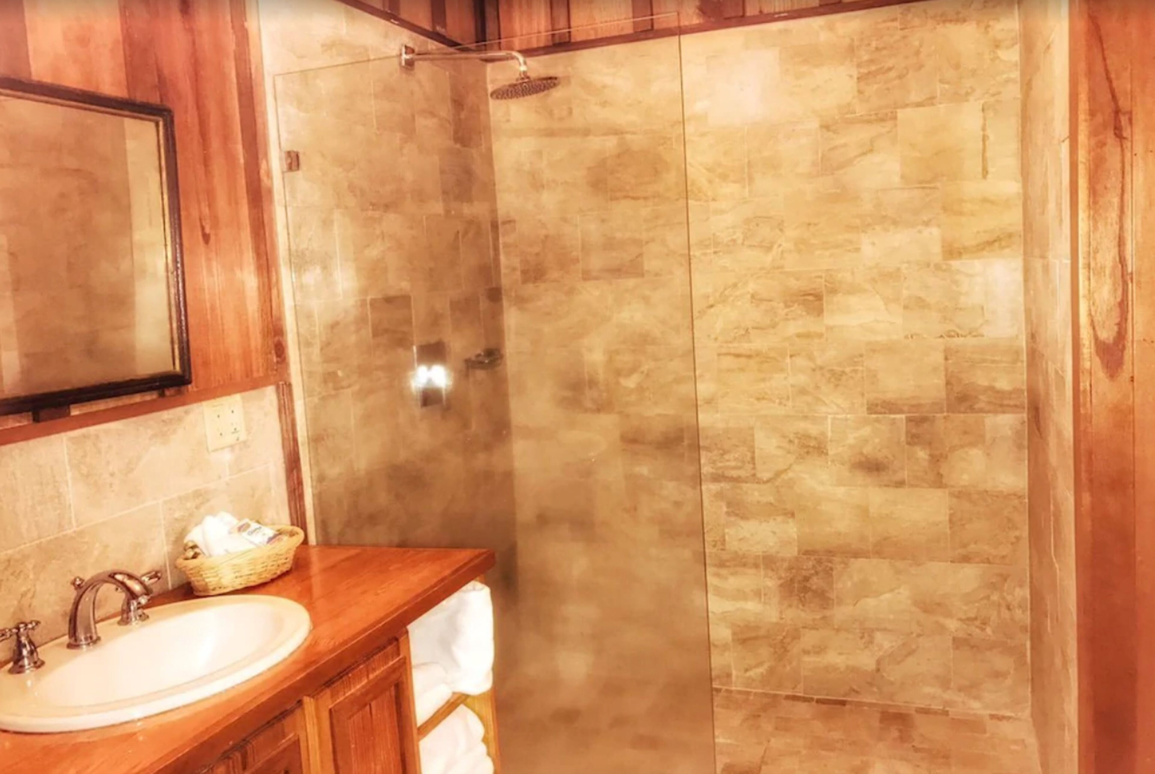 A bathroom with a wooden vanity, a sink, and a shower with beige tiles.