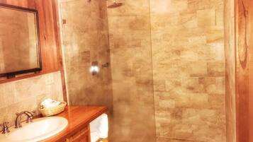 A bathroom with a wooden vanity, a sink, and a shower with beige tiles.