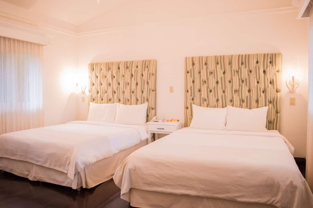 A hotel room with two beds, a nightstand, and a lamp.