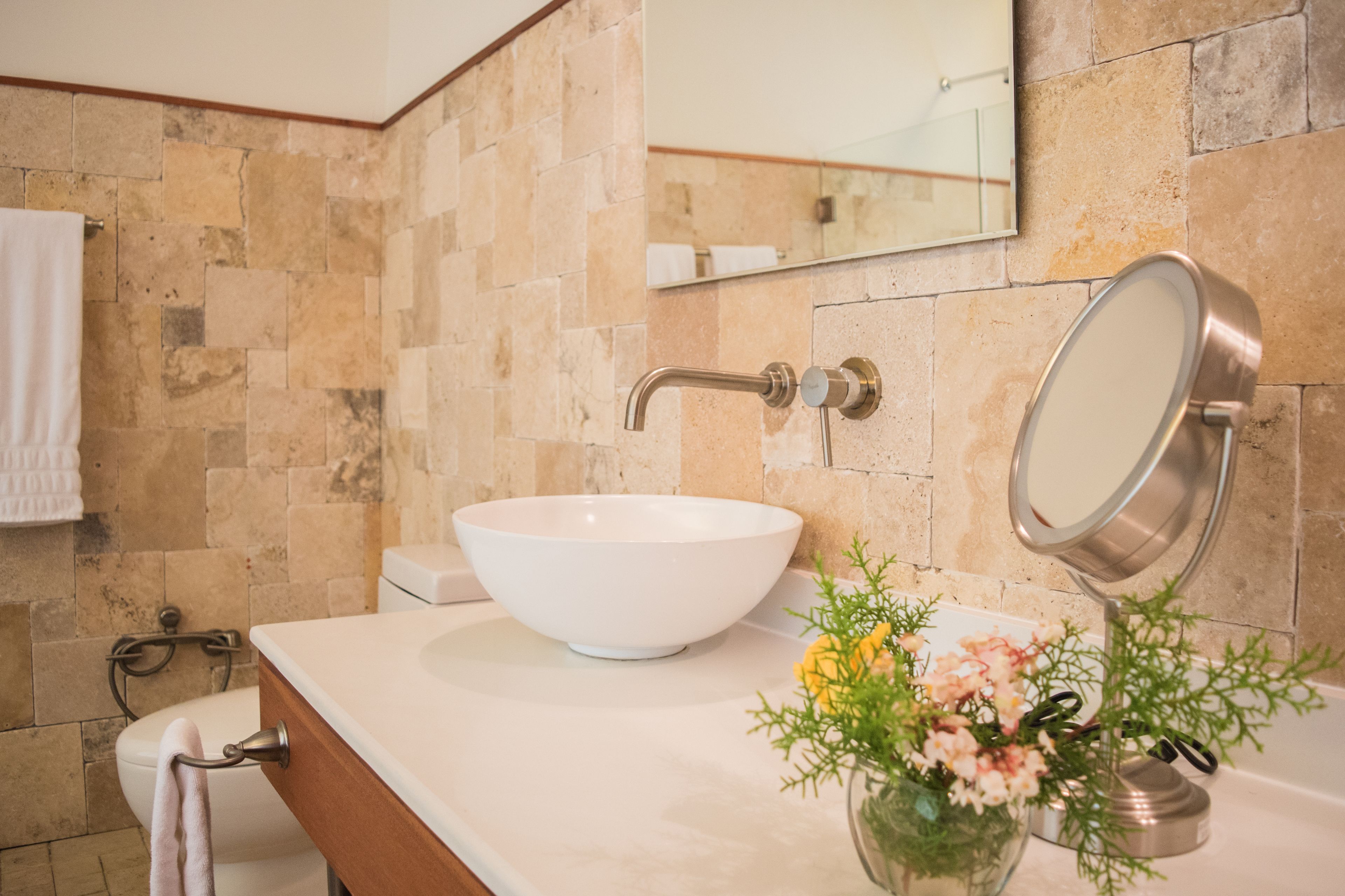 Un baño con un lavabo blanco, un espejo y un florero con flores.