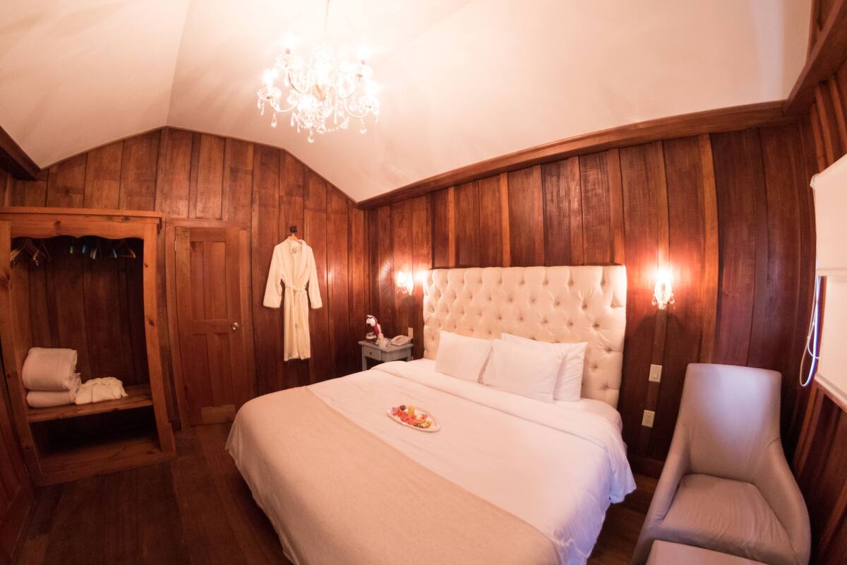 A bedroom with a large bed, a chair, a robe hanging, and a coat rack.