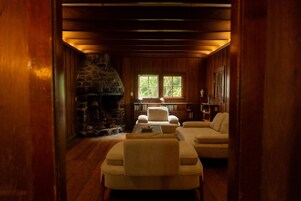Una habitación acogedora con chimenea de piedra, paredes de madera y una zona de estar con sofá y sillones.