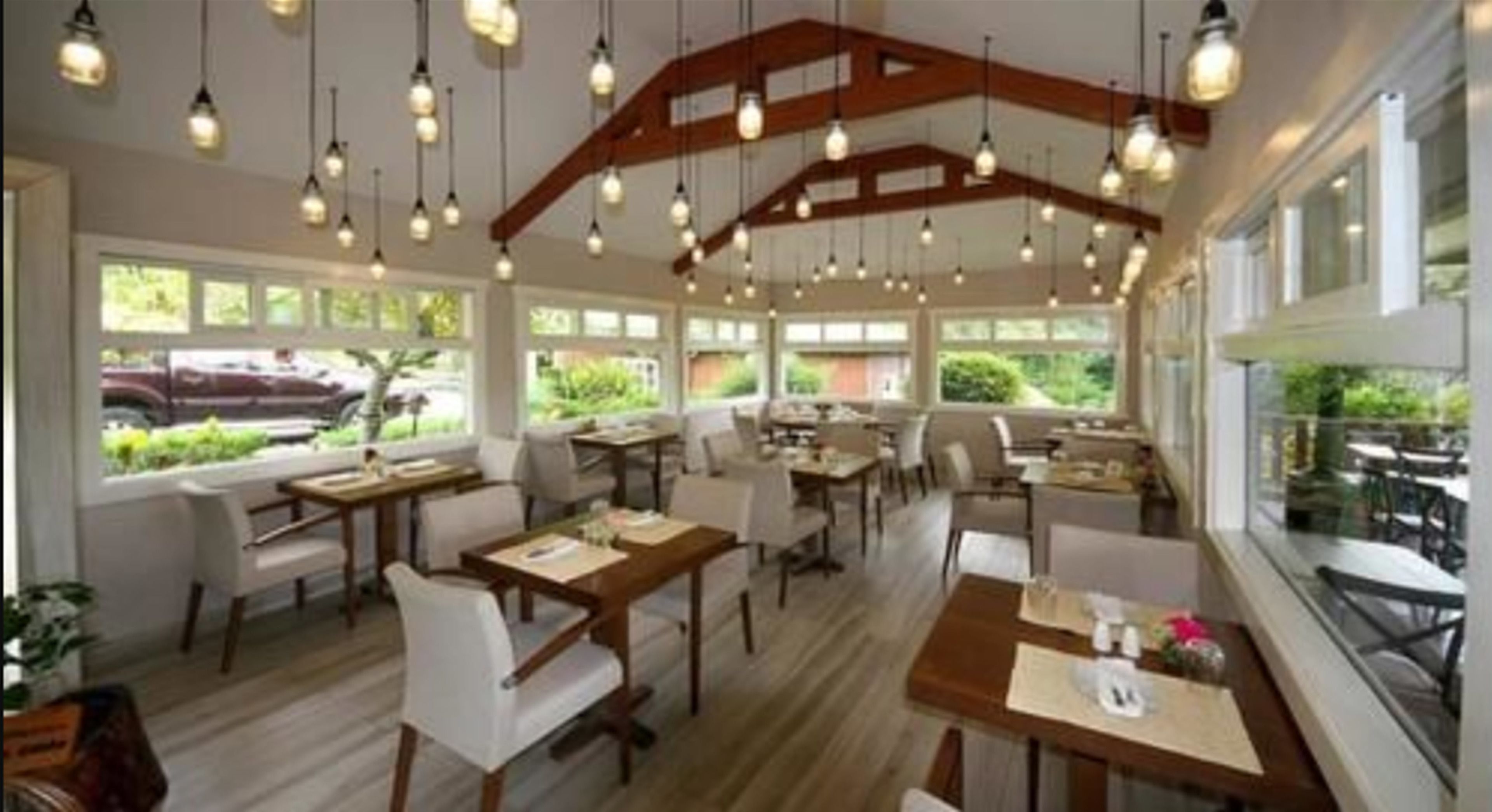 Un restaurante con varias mesas y sillas, vigas de madera en el techo y grandes ventanales con vistas al exterior.