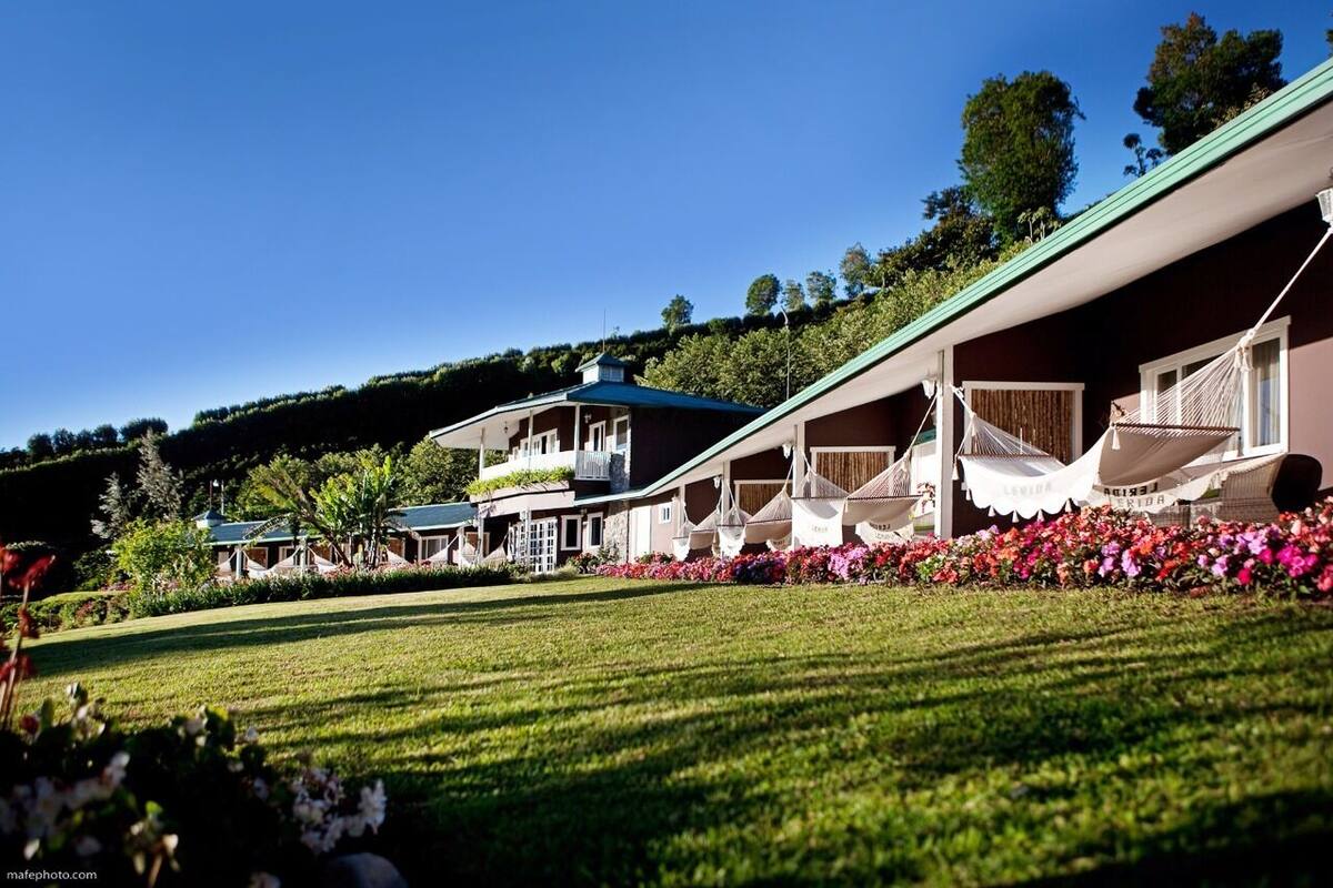 A row of single-story buildings with balconies, surrounded by well-maintained gardens and a clear blue sky.