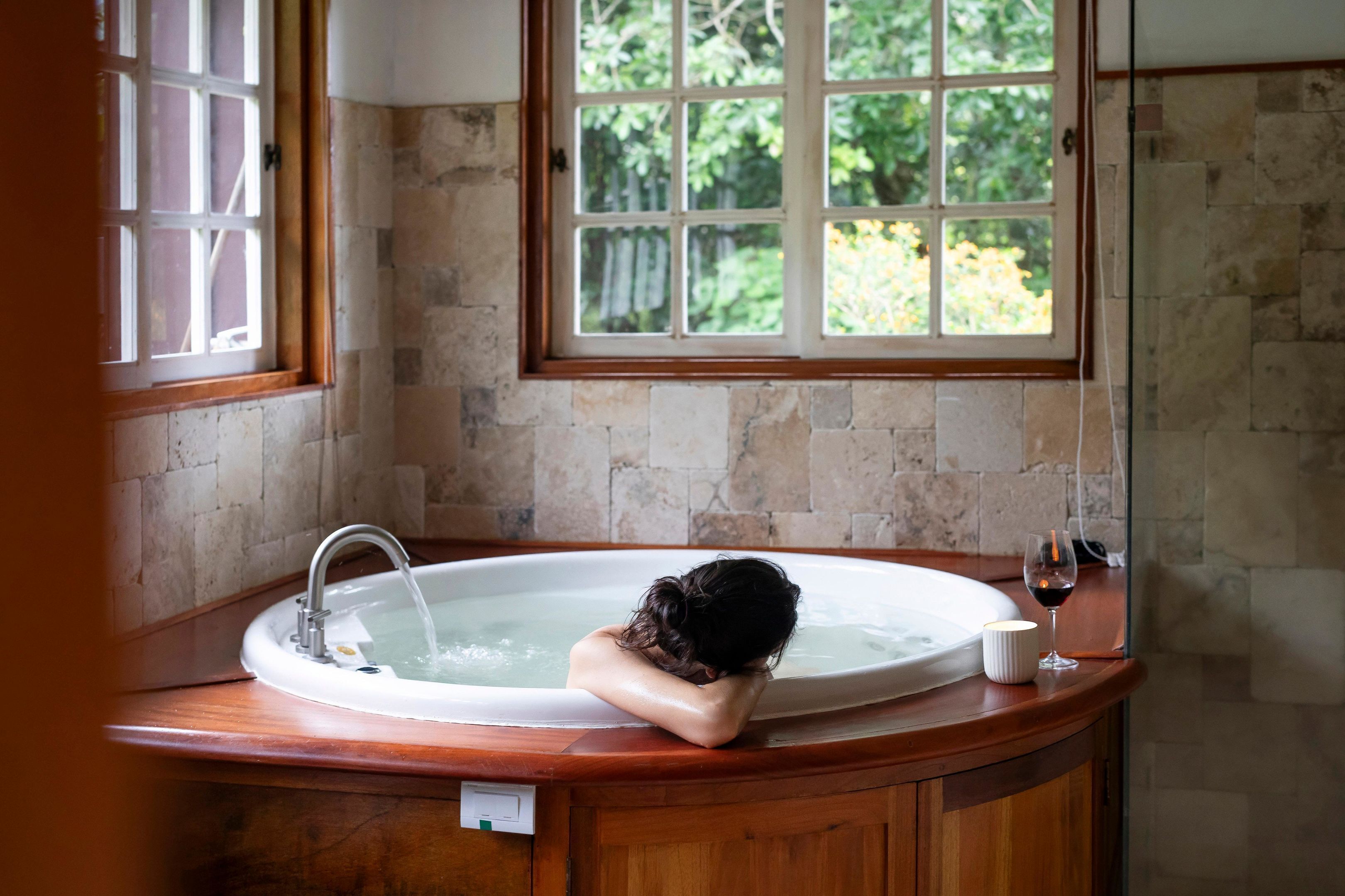 Una persona relajándose en una bañera con vistas a la vegetación desde la ventana.