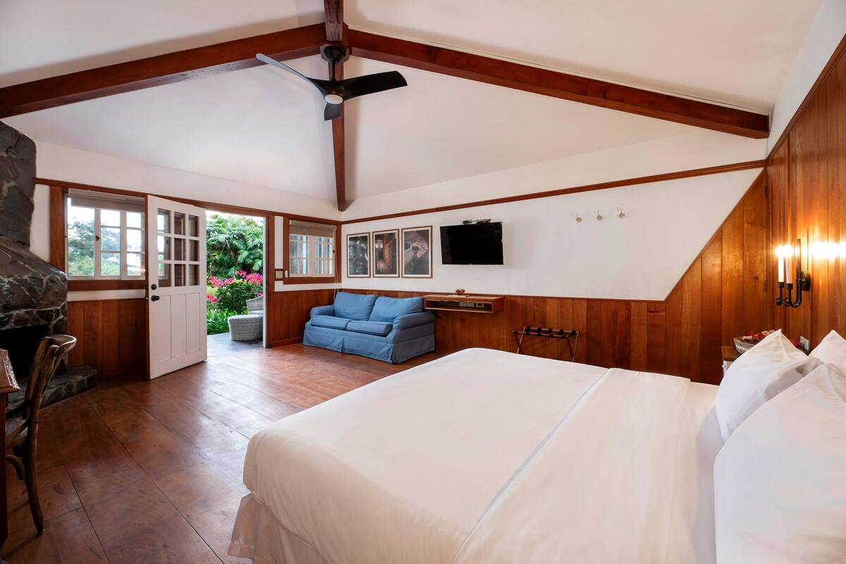 A bedroom with a large bed, a blue sofa, a fireplace, and a TV on the wall.