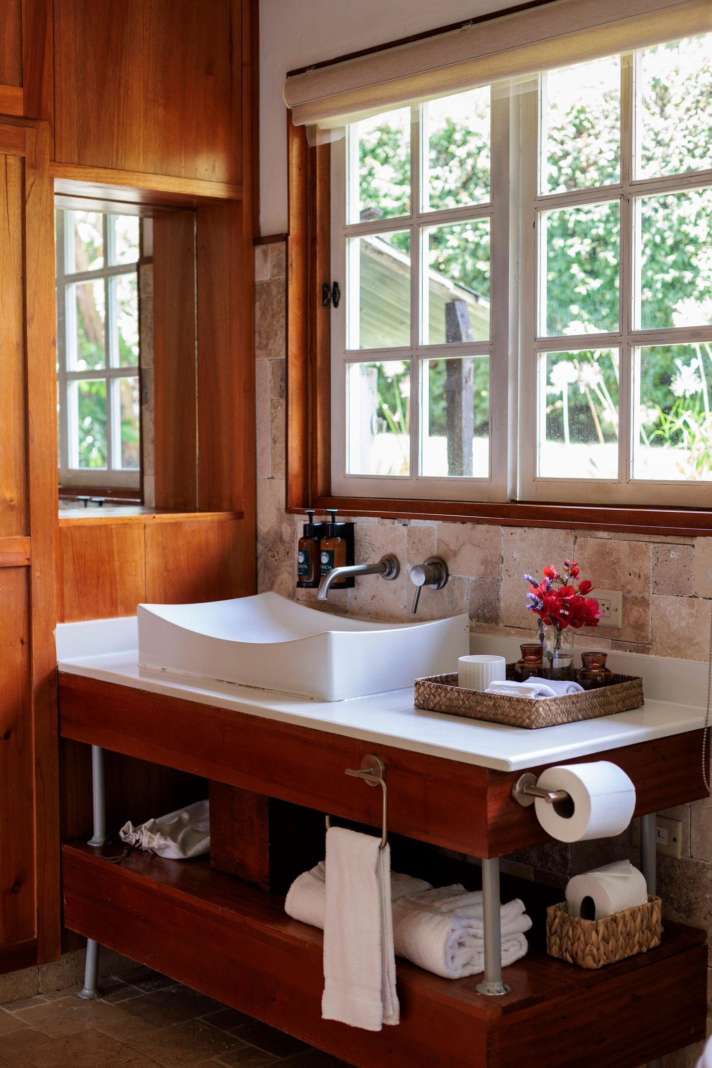 Une salle de bain avec un meuble-lavabo en bois, un lavabo blanc et une fenêtre donnant sur un paysage verdoyant.