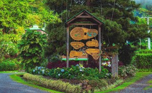 A wooden sign with multiple labels indicating various amenities such as a coffee plantation, senderismo, tours, and a reception area. - Hotel Finca Lerida (Los Naranjos)