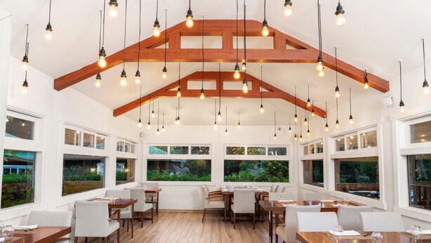 A spacious dining area with wooden beams and hanging light fixtures, large windows with views of greenery, and neatly arranged tables and chairs. - Hotel Finca Lerida (Los Naranjos)