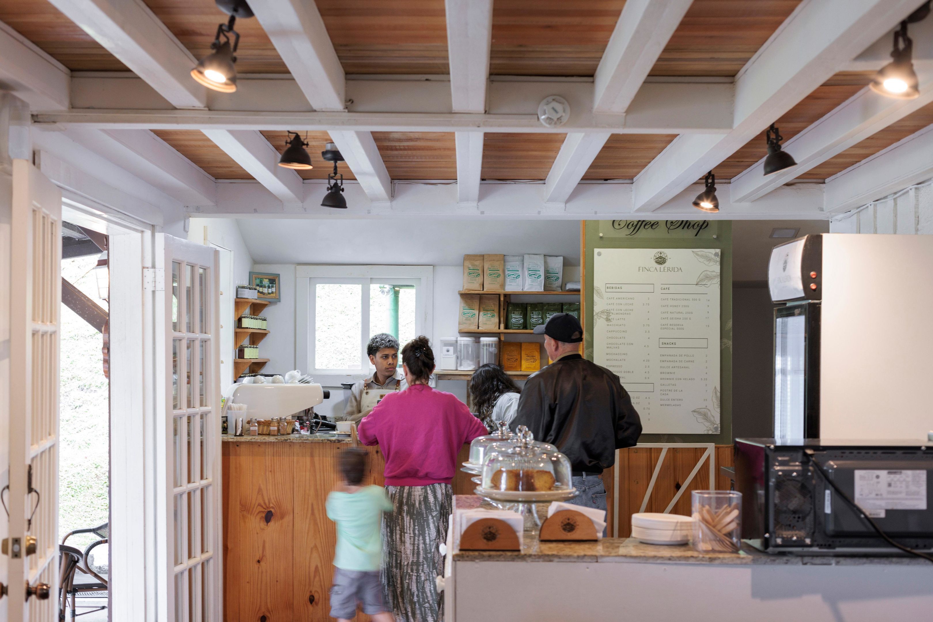 A café interior with wooden beams, a counter with pastries, and a menu board.