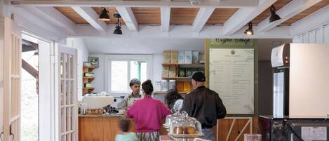 A café interior with wooden beams, a counter with pastries, and a menu board.