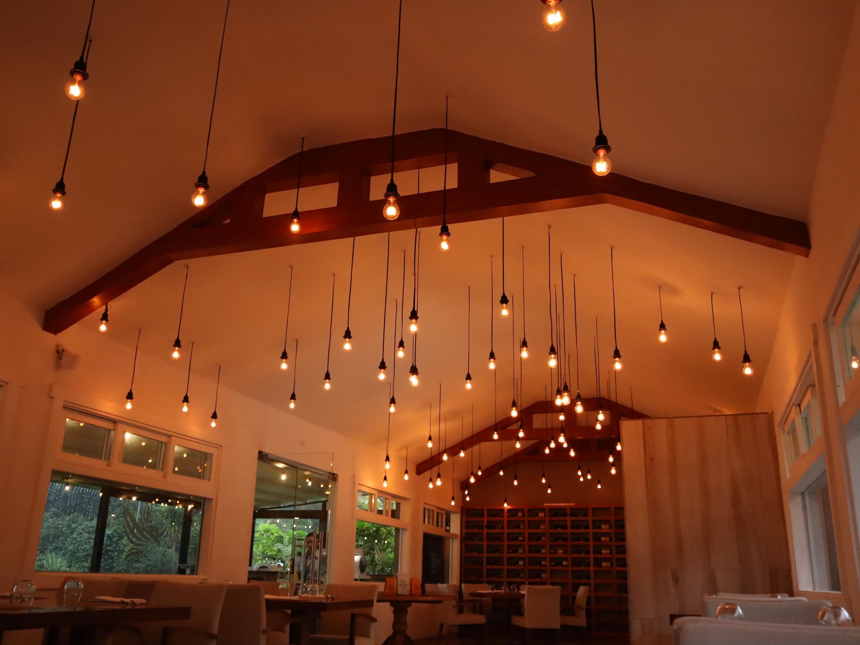 A dining area with hanging light fixtures, wooden beams, and large windows with views of greenery.