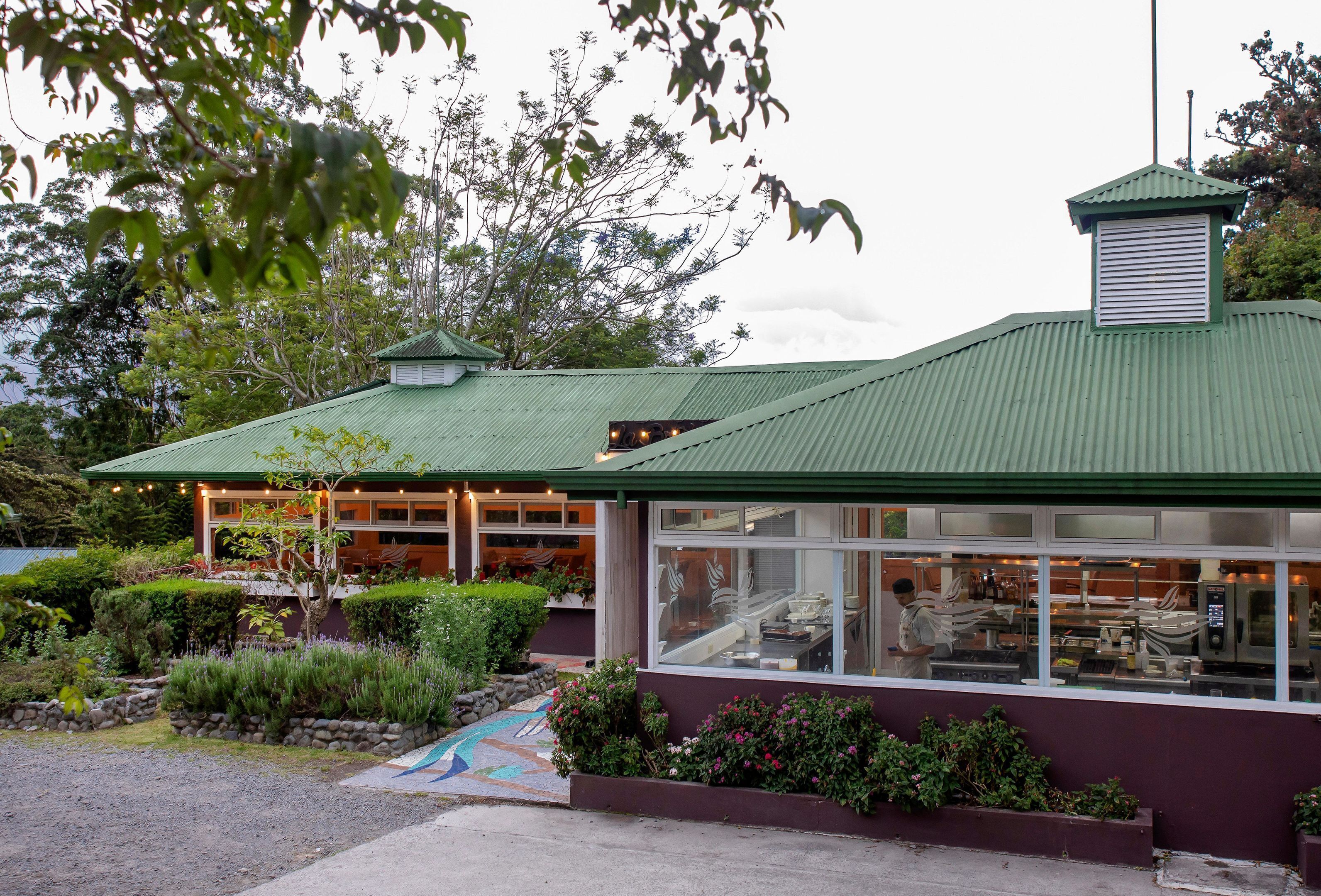 A building with a green roof, large windows, and a garden area with plants and a pathway.