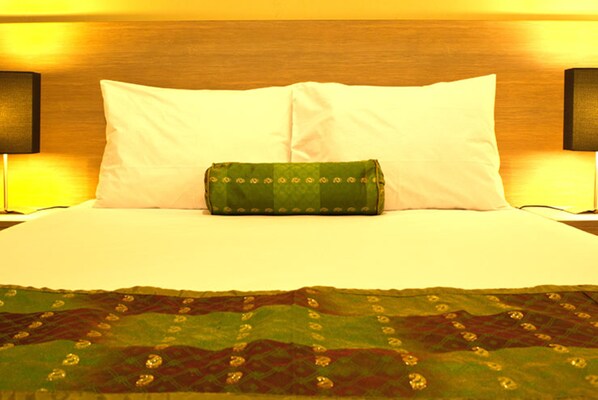 A bed with white pillows and a green decorative pillow, a wooden headboard, and a green patterned bedspread.