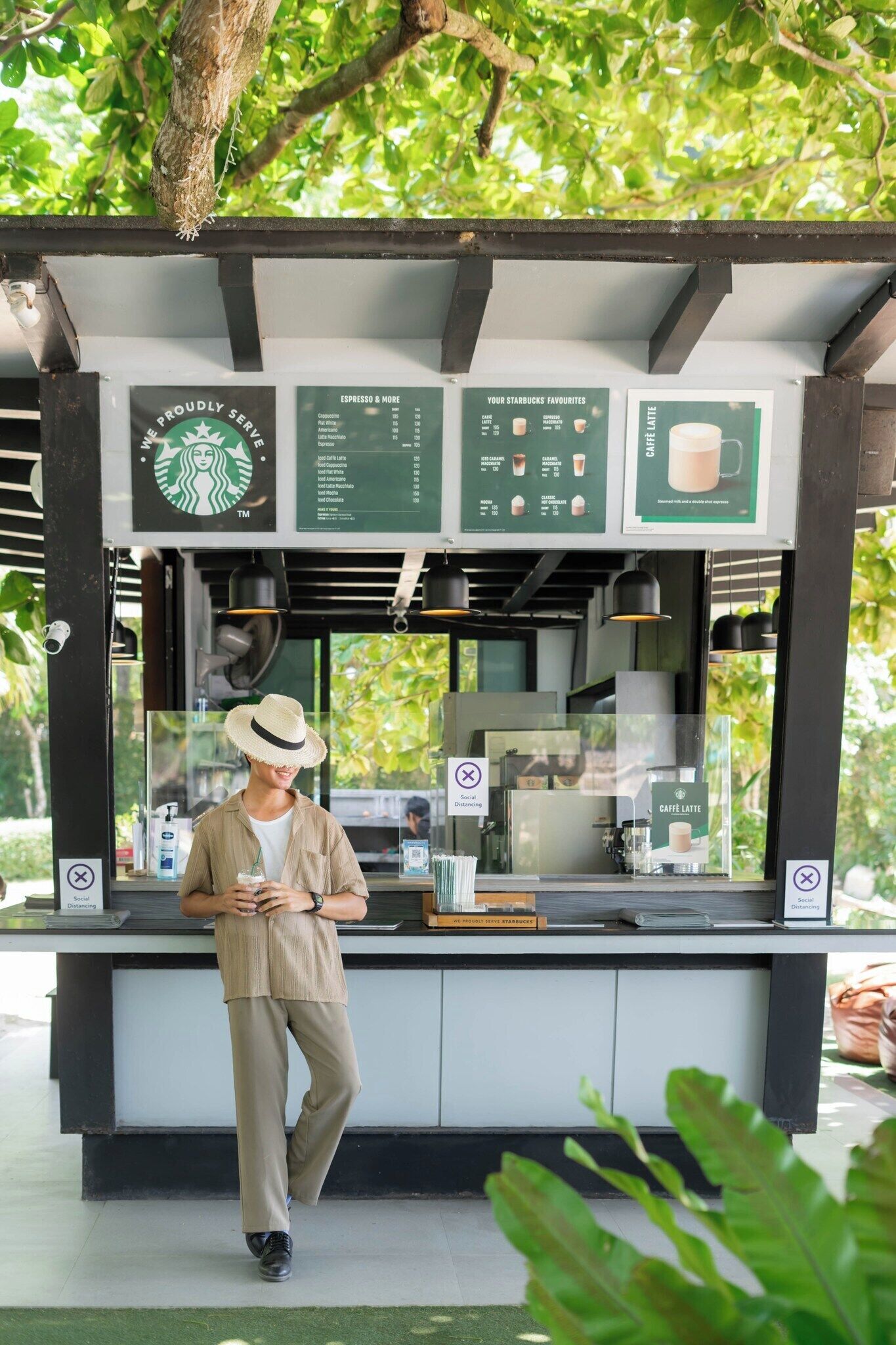 A Starbucks kiosk with a menu board, a coffee machine, and a person standing in front.