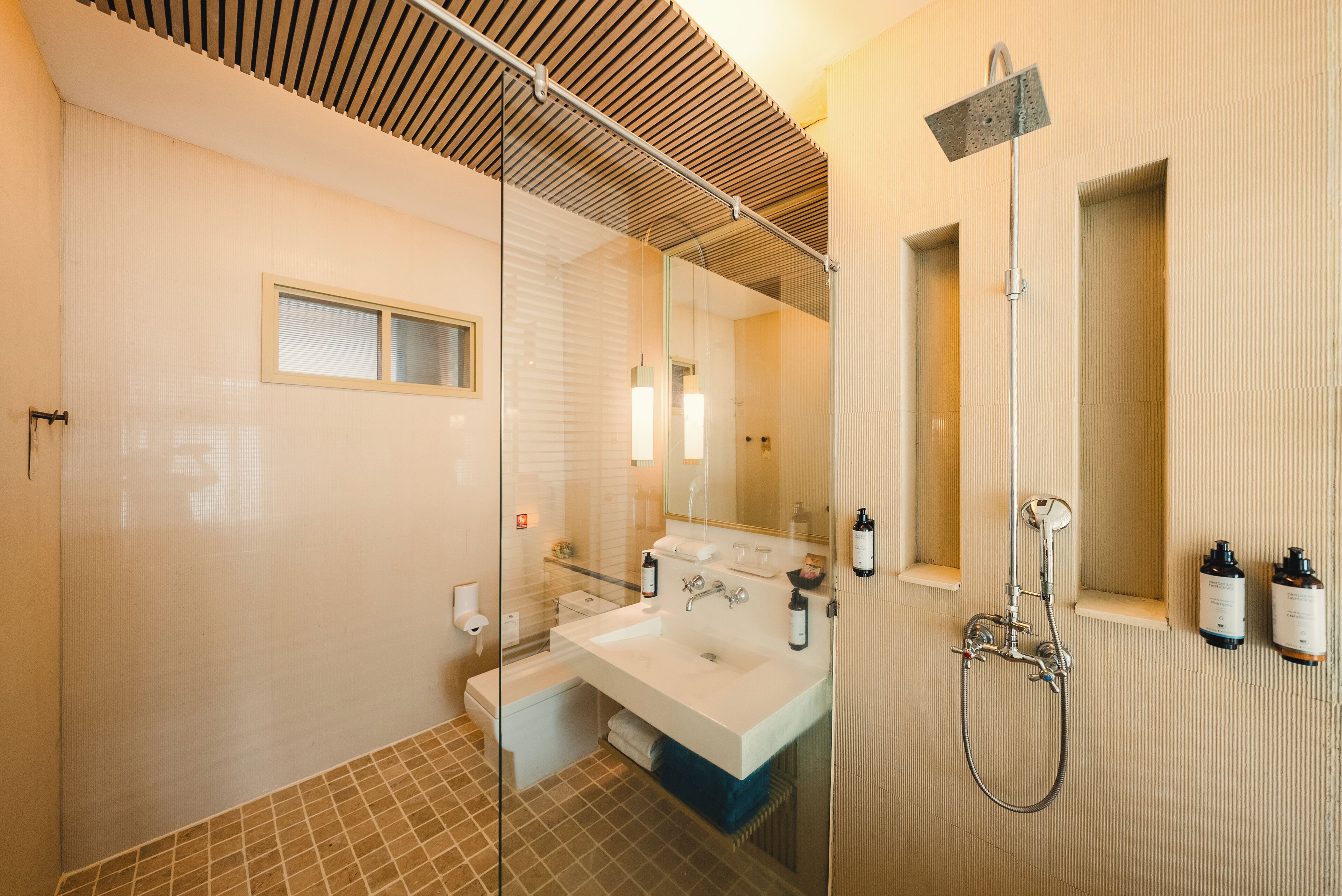 Un baño moderno con un espejo grande, un lavabo blanco, ducha y zona de ducha con mampara de cristal.