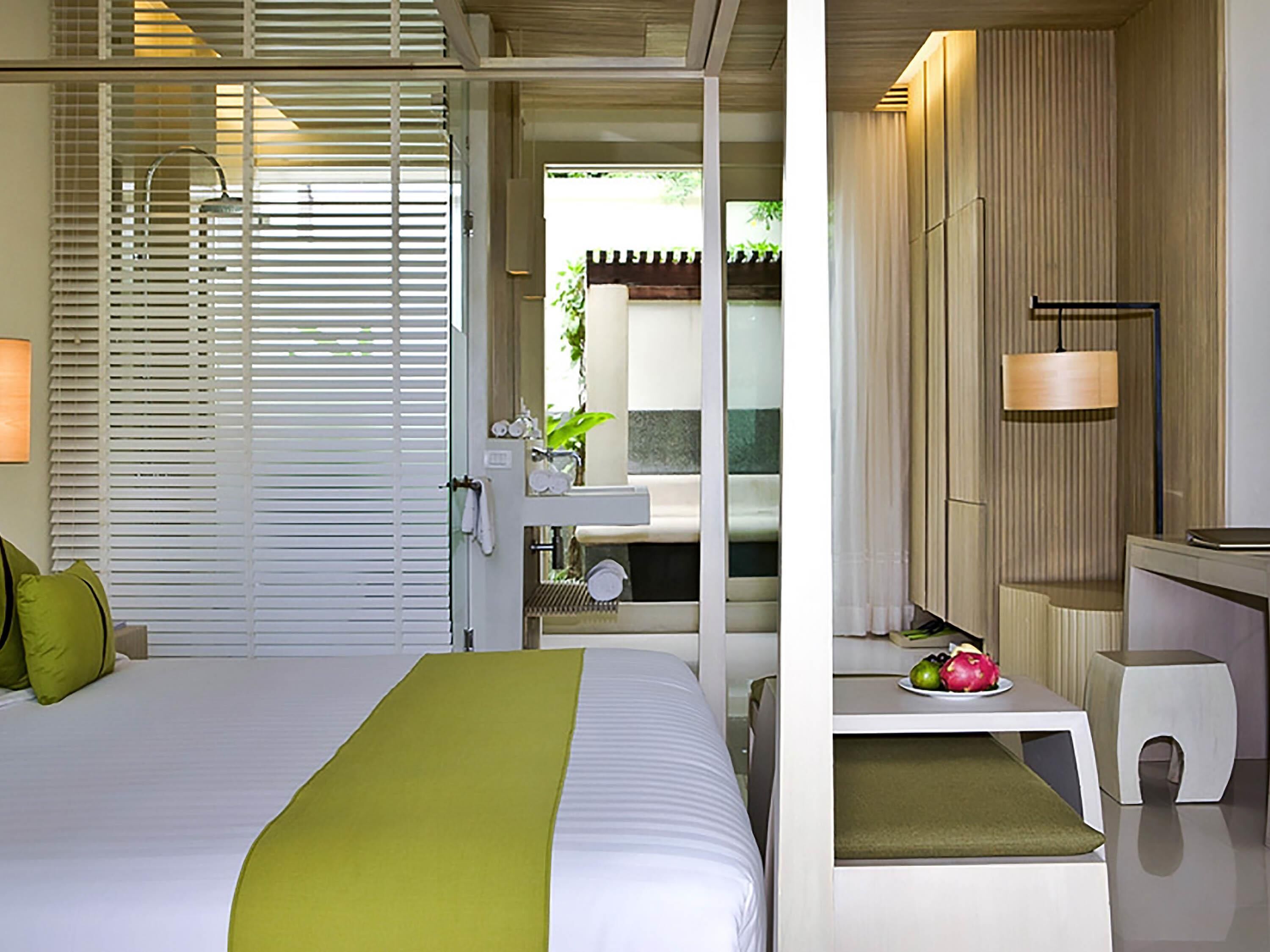 A hotel room with a bed, a bathroom with a sink, and a small table with fruit.