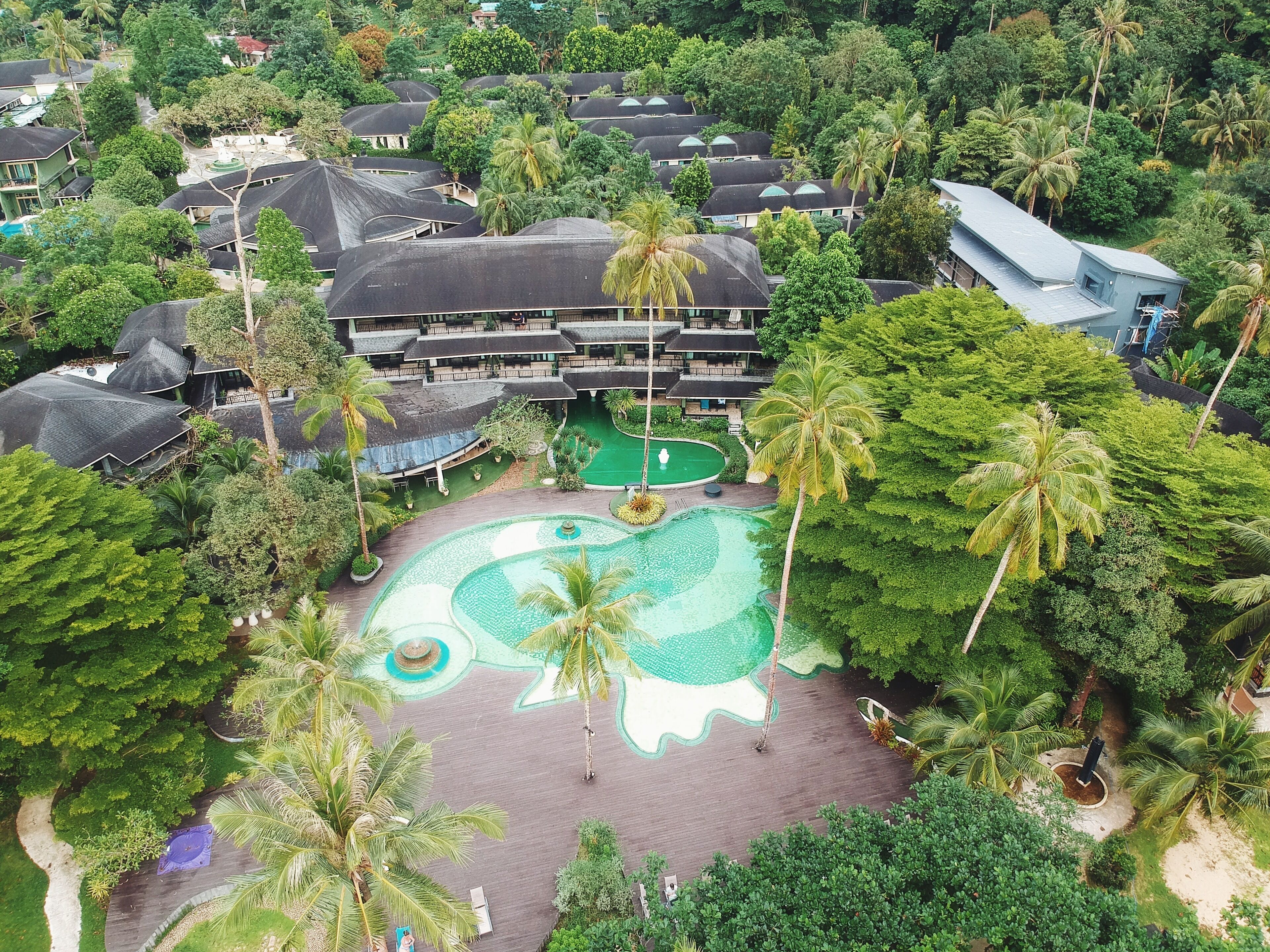 Eine Luftaufnahme eines Resorts mit mehreren Gebäuden, einem zentralen Poolbereich und üppiger, umgebender Vegetation.