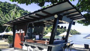 A bar area with a counter, stools, and umbrellas, overlooking a body of water.