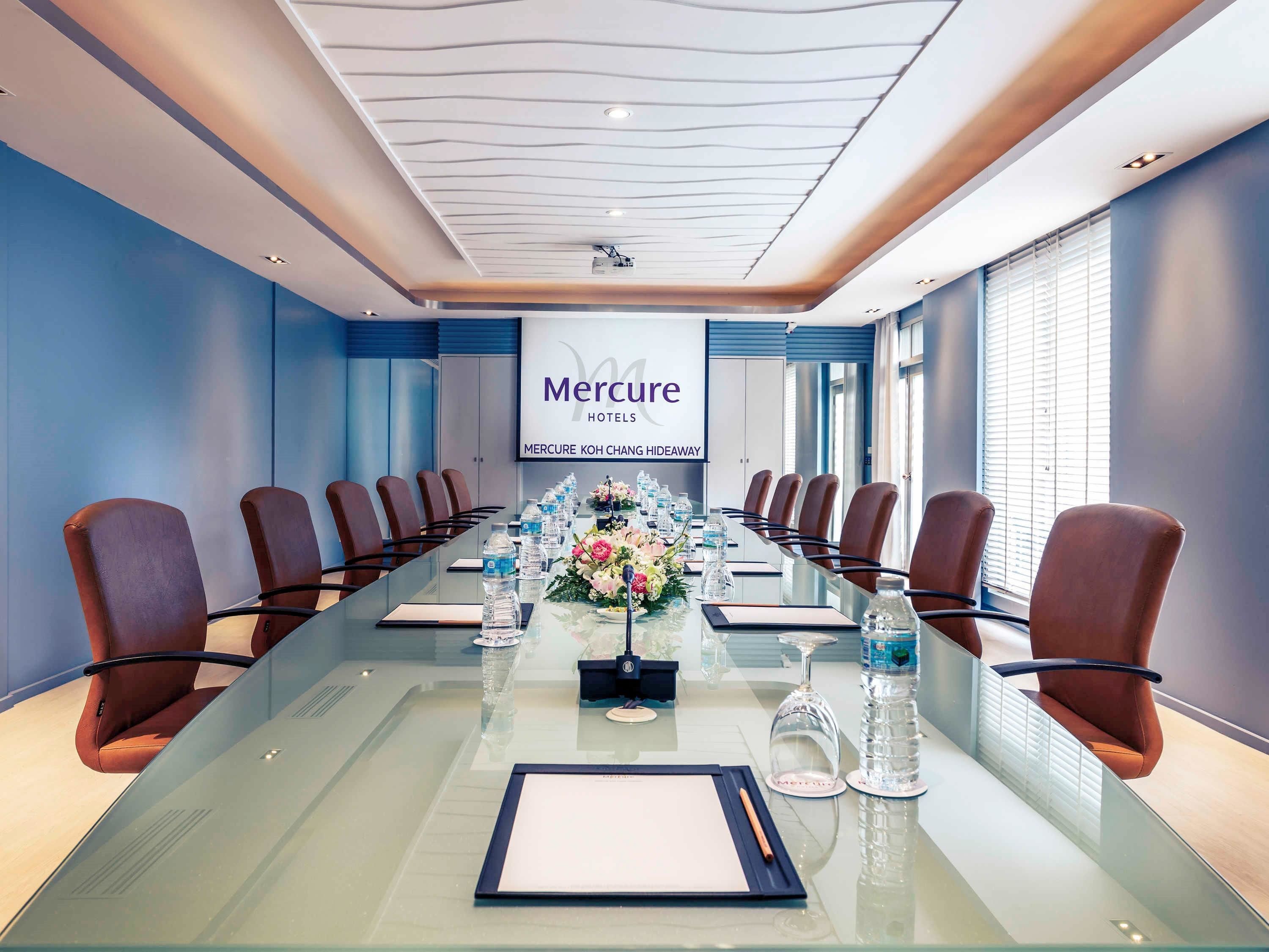 A conference room with a long table, chairs, water bottles, and a floral centerpiece.