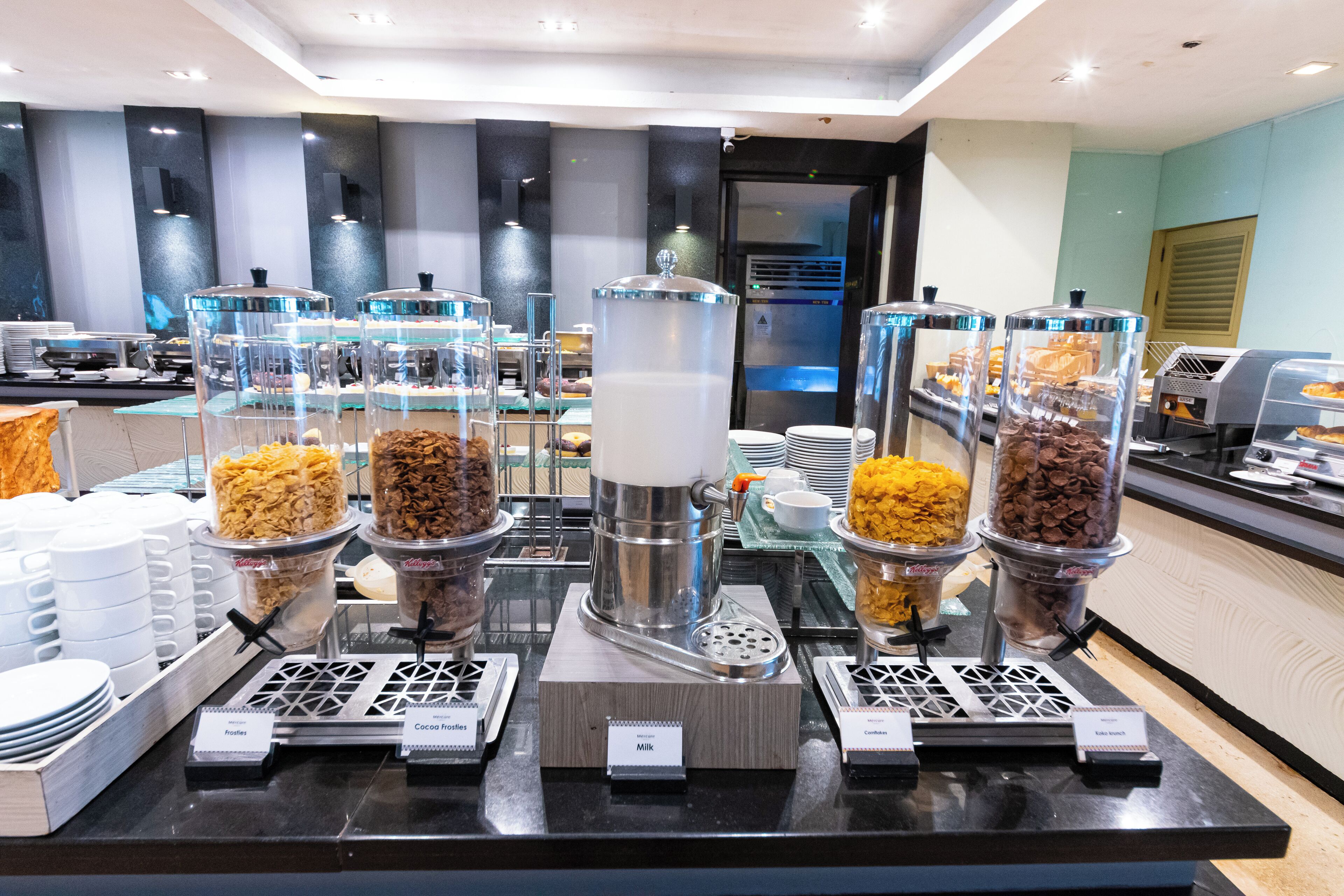 A buffet area with various food dispensers, including options for milk, cocoa, and other beverages.