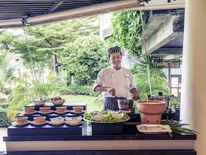 A chef preparing food at an outdoor counter with a variety of dishes and a large clay pot. - Mercure Koh Chang Hideaway (Ko Chang)
