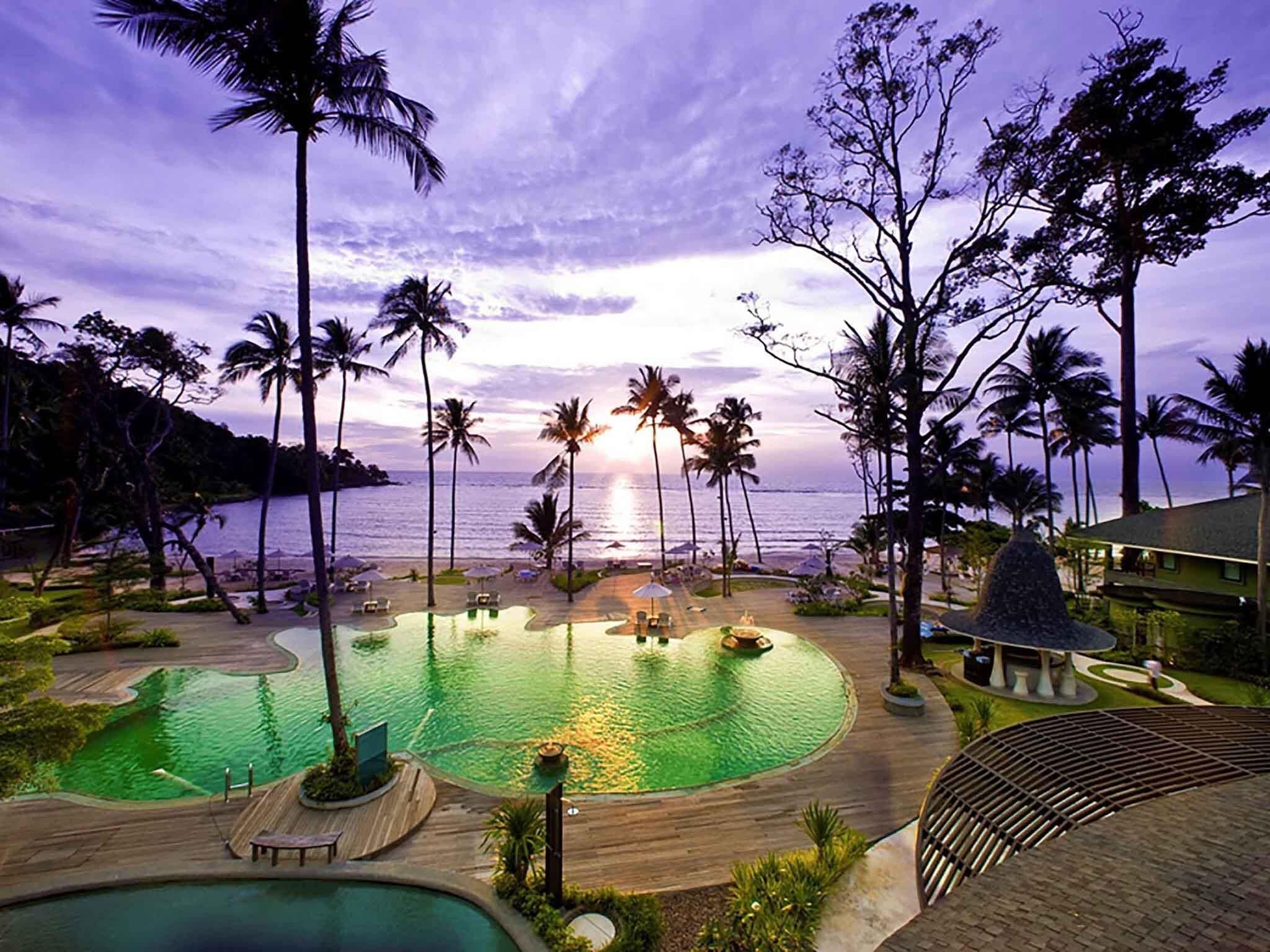 Un resort con piscina, palmeras y vista al océano.