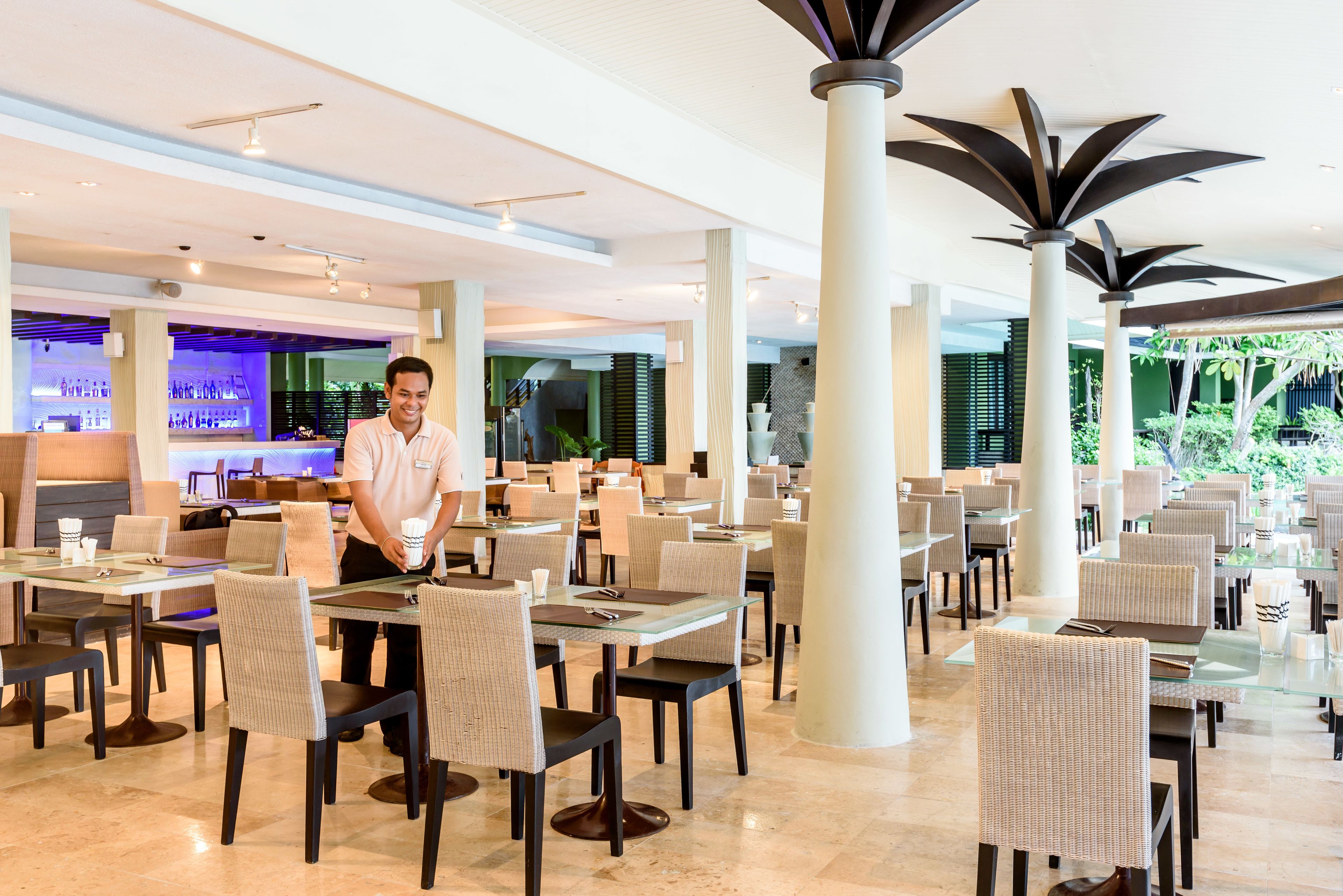 A spacious restaurant with high tables and chairs, a bar area in the background, and large pillars.