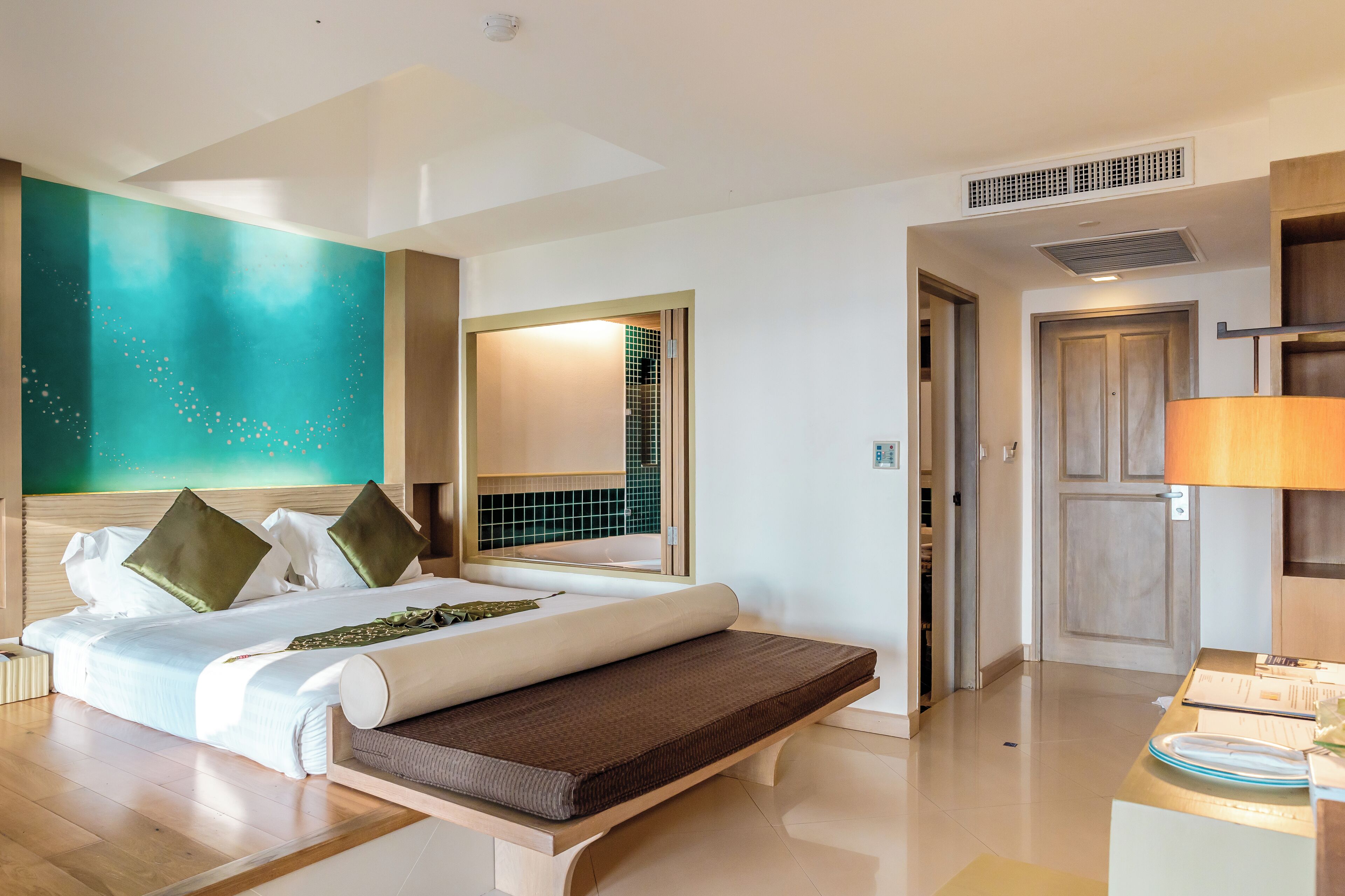 Habitación de hotel moderna con una cama grande, una mesita de noche, un espejo y vistas al pasillo.
