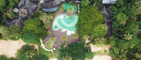 An aerial view of a resort with a swimming pool, beach, and lush greenery.