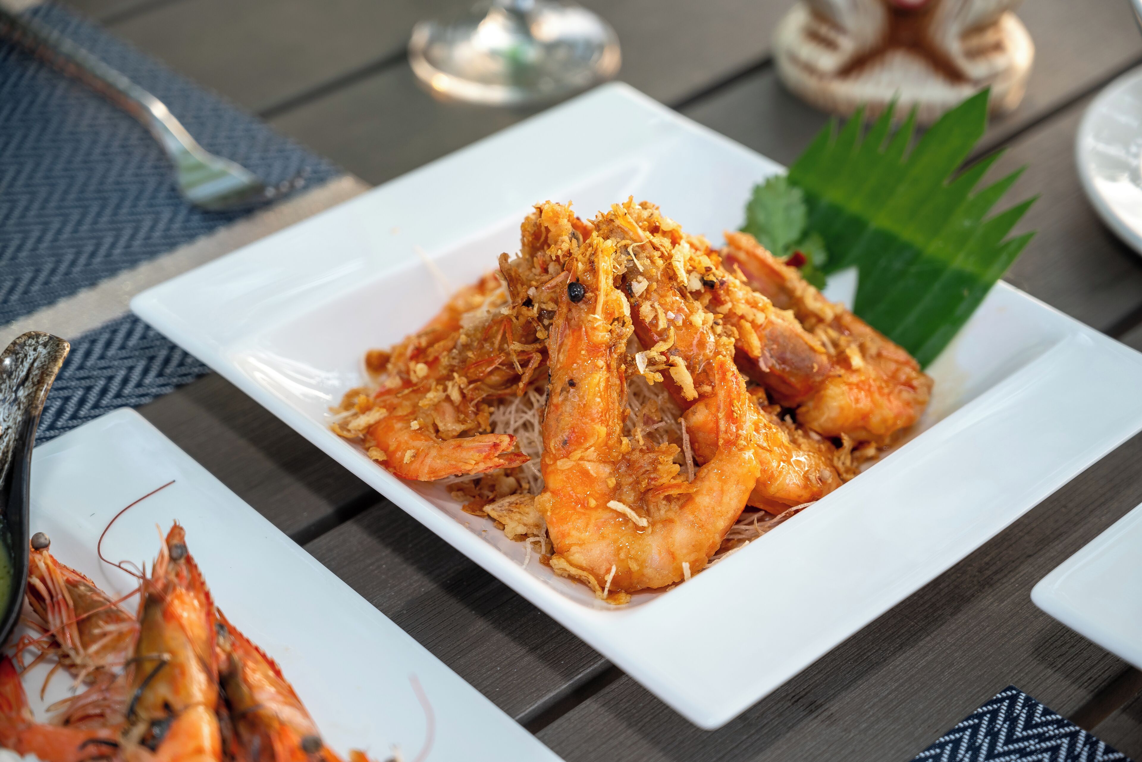 A plate of cooked shrimp on a white rectangular plate, accompanied by a fork and a decorative leaf.