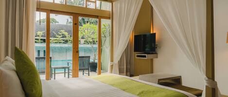 A bedroom with a bed, a TV, a desk, and a view of a pool and greenery.