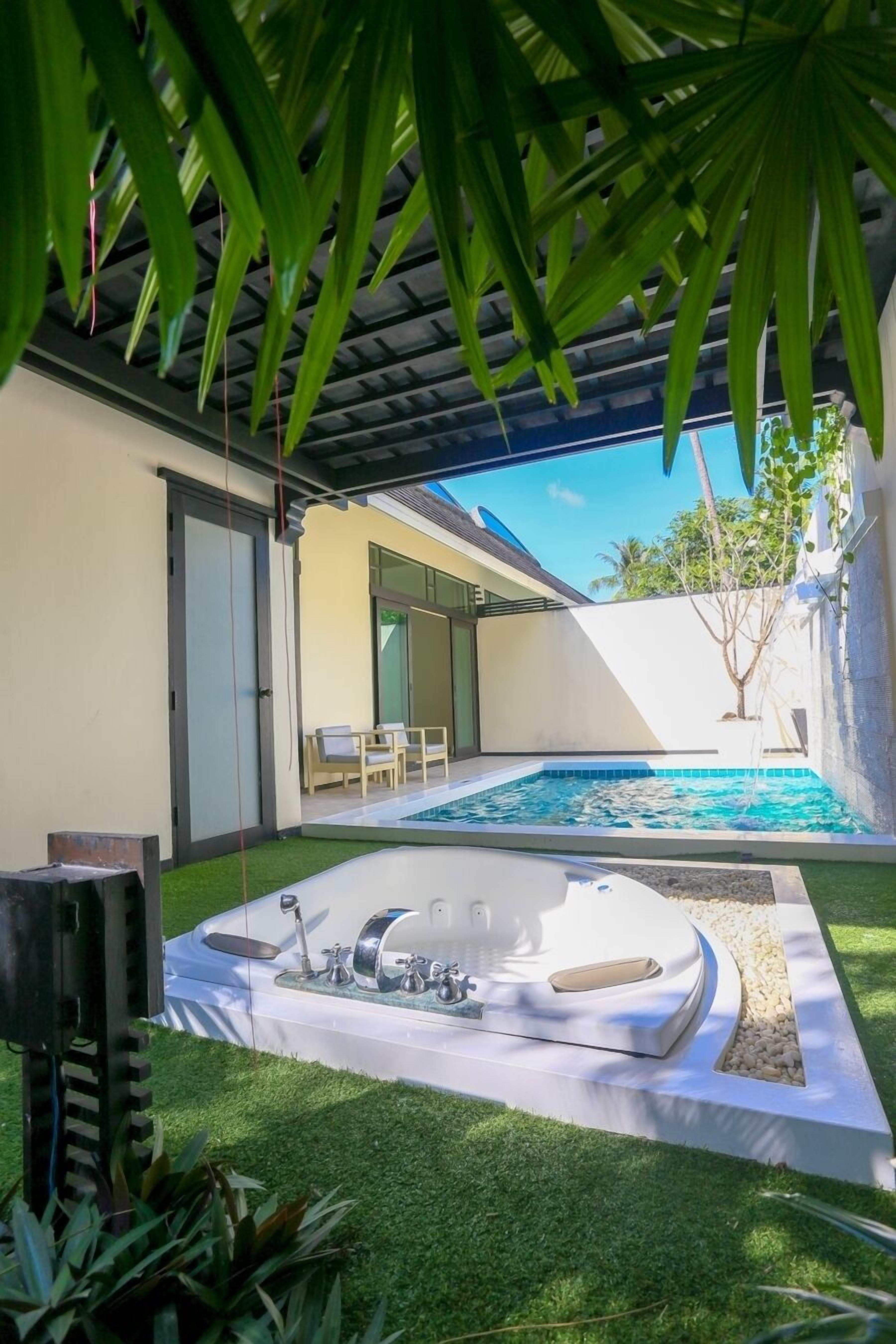 A modern outdoor pool area with a hot tub, surrounded by a well-maintained lawn and a covered patio.