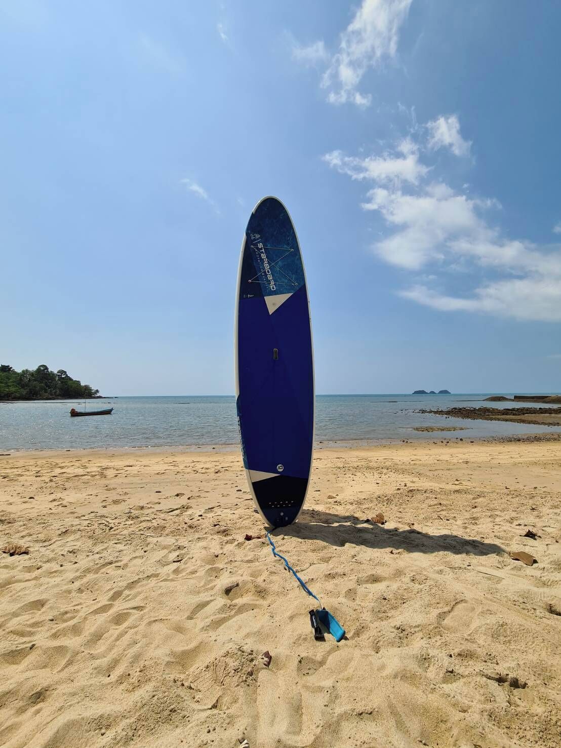 A surfboard on a sandy beach with a calm sea and a clear sky in the background.