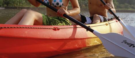 Two people in a red kayak on a calm body of water with dense greenery in the background.