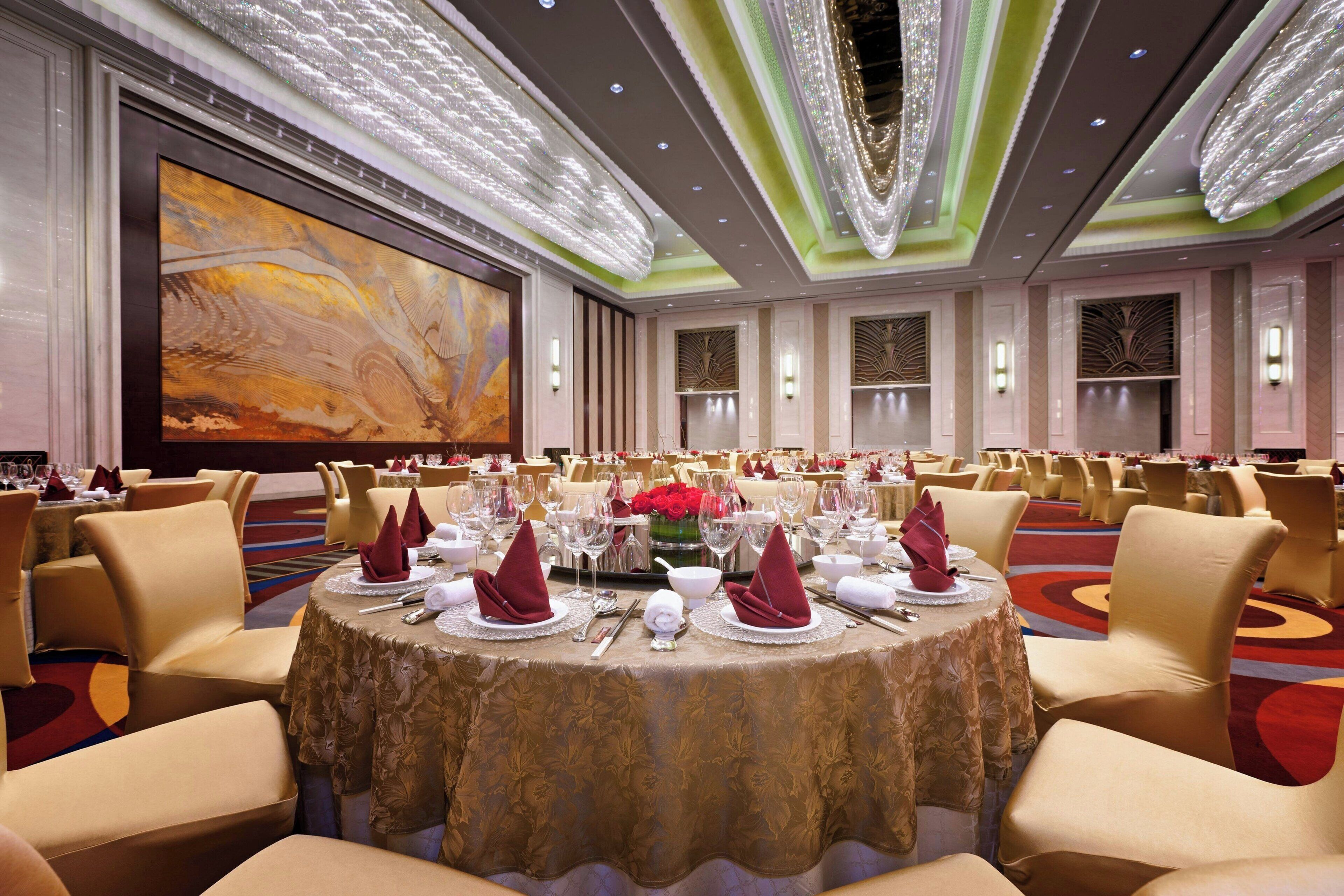 Een feestzaal met ronde tafels gedekt voor een diner, voorzien van stoelen, tafellinnen en servies.