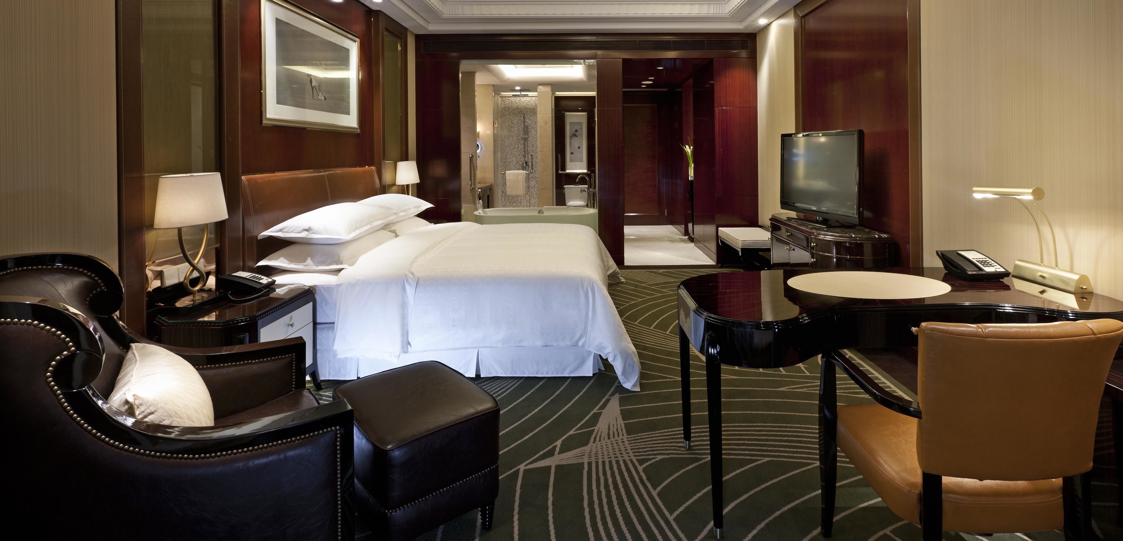 Habitación de hotel con una cama grande, un escritorio con una silla, televisión y un baño a la vista.