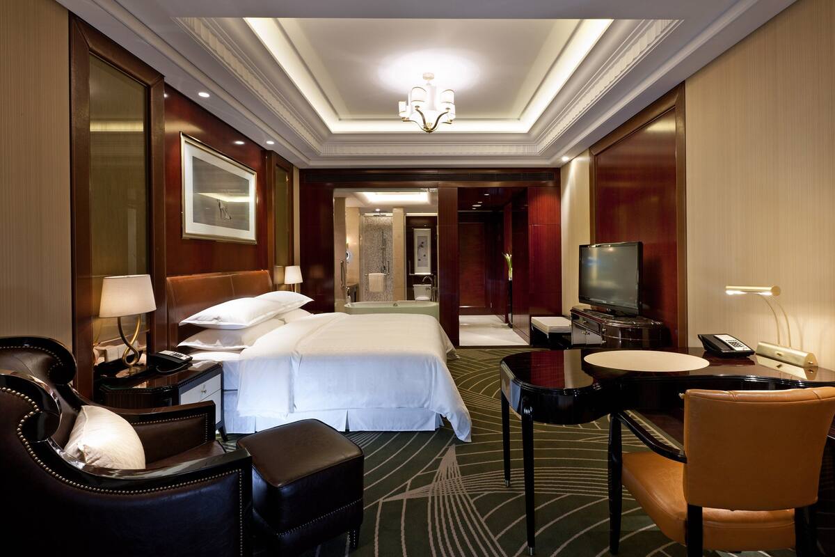 Habitación de hotel con una cama grande, un escritorio con una silla, televisión y un baño a la vista.