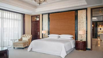A spacious hotel room with a large bed, a sitting armchair, a small table, and a chandelier.