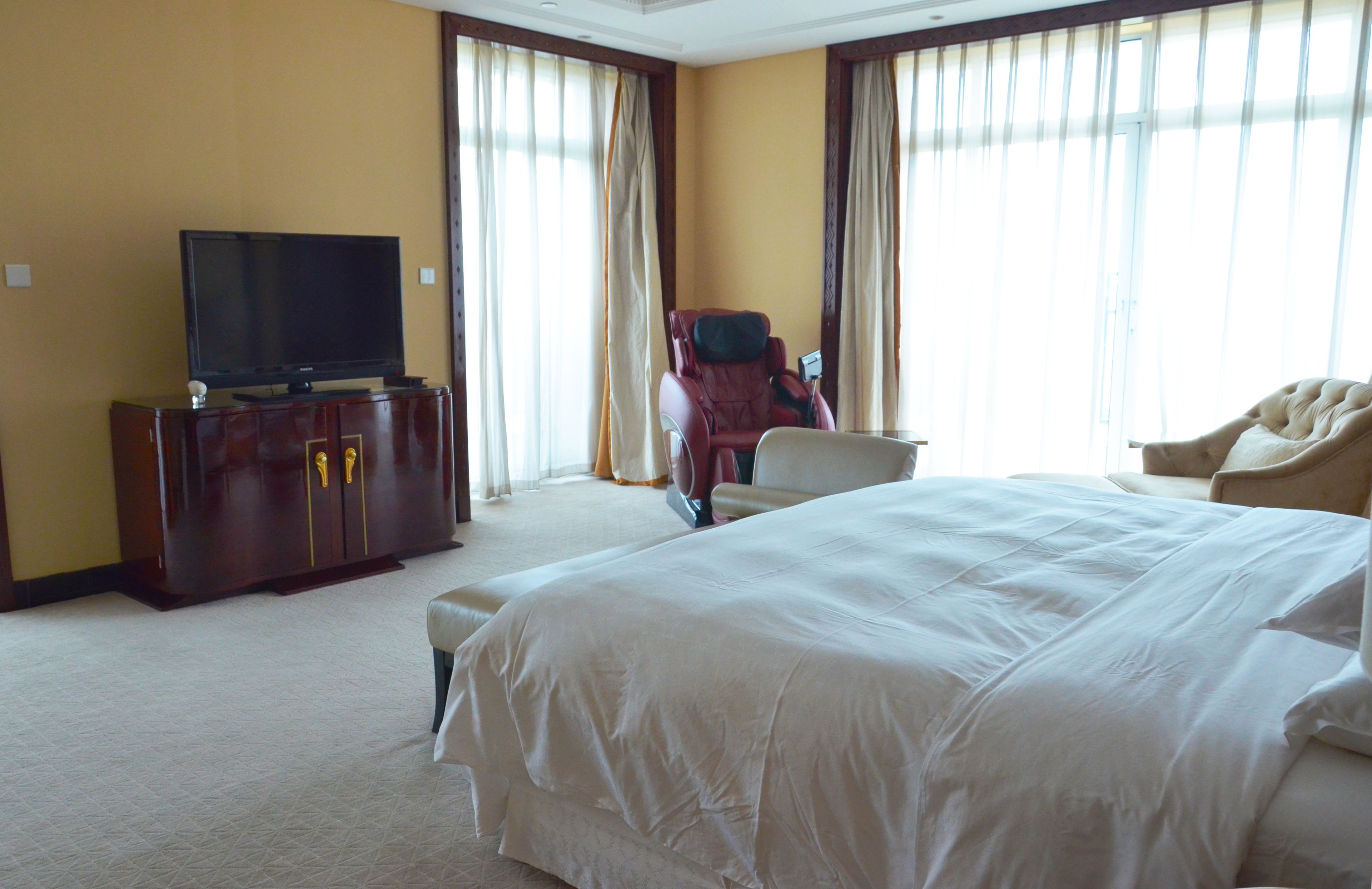 Ein Hotelzimmer mit einem großen Bett, einem Fernseher auf einer Holzkommode, einem Massagesessel und einem Sofa.