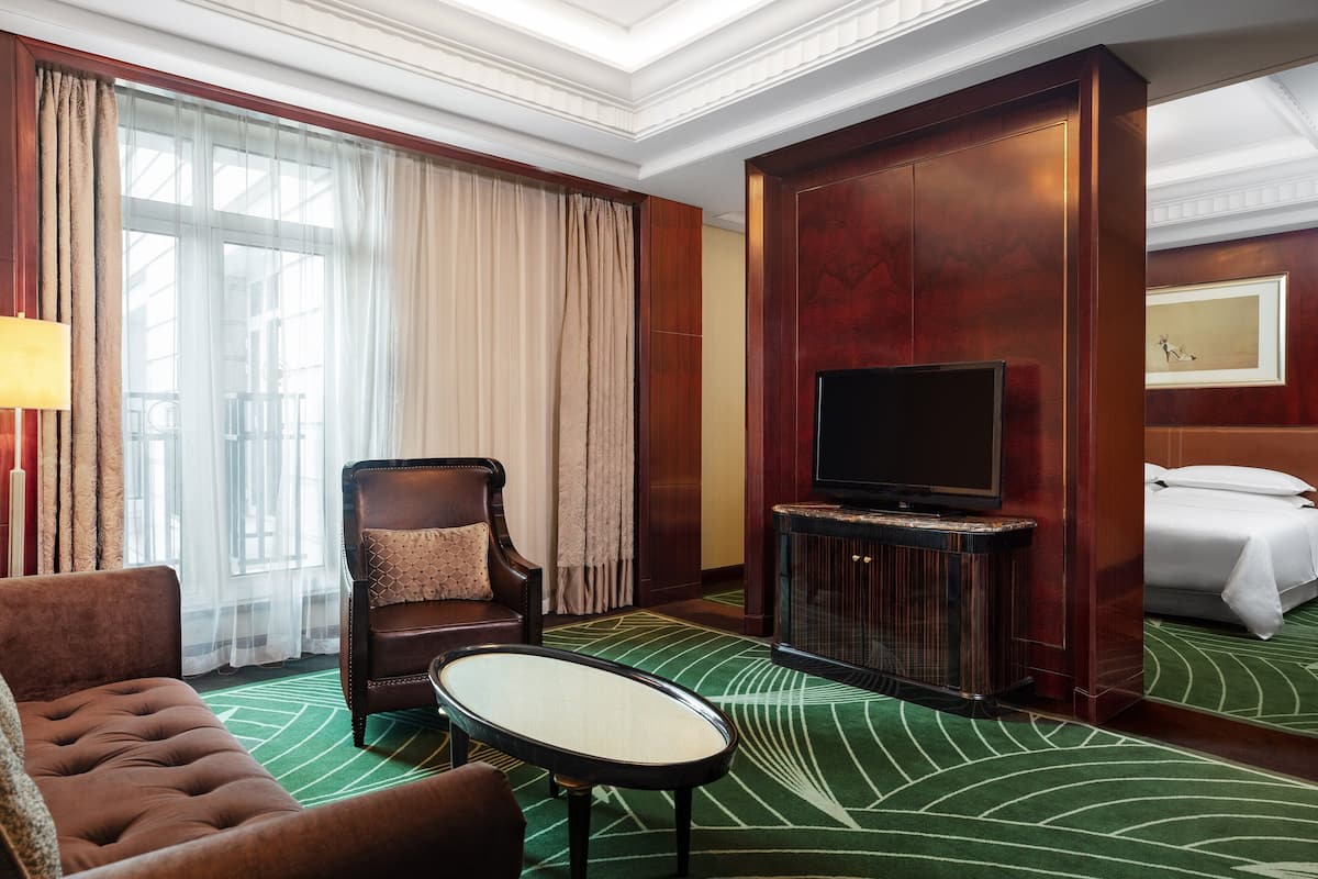 Una habitación de hotel con un ventanal grande, un sofá, una silla, un televisor y una cama.