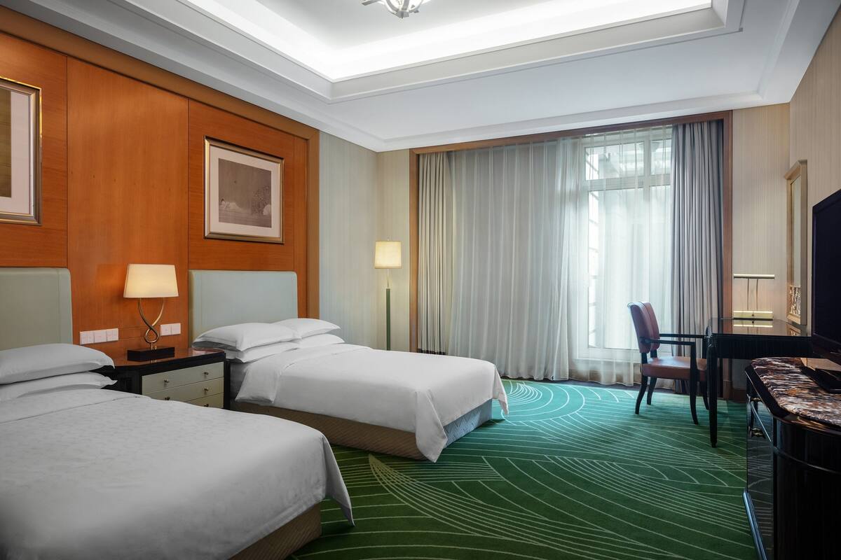 Una habitación de hotel con dos camas, un escritorio, una silla y un televisor.