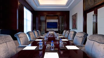 Un salón de conferencias con una larga mesa, varias sillas, botellas de agua y una pantalla de televisión.