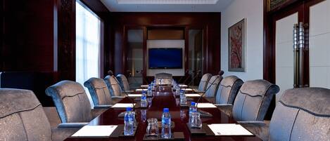 Un salón de conferencias con una larga mesa, varias sillas, botellas de agua y una pantalla de televisión.