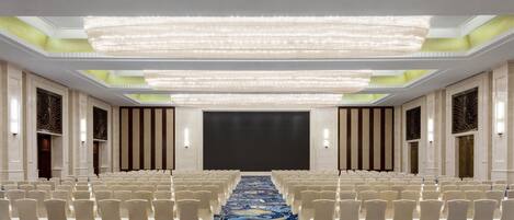 A conference room with rows of white chairs, a patterned carpet, and a large screen at the front.