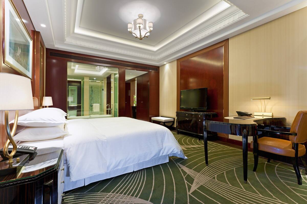 Habitación de hotel con una cama grande, un escritorio con silla, un televisor y un espejo.
