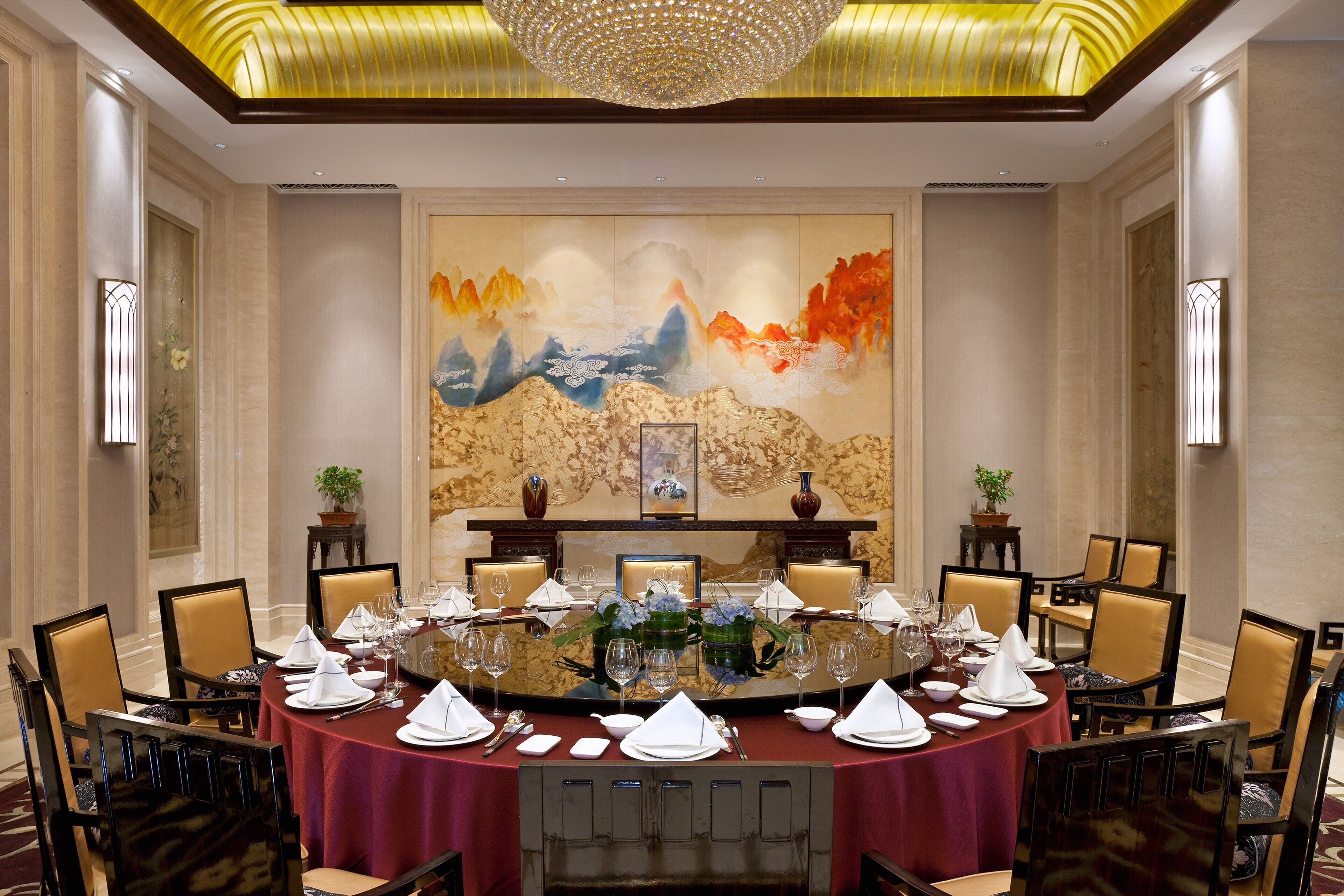 Uma sala de jantar formal com uma mesa redonda posta para refeição, ladeada por cadeiras, e um grande quadro abstrato na parede.