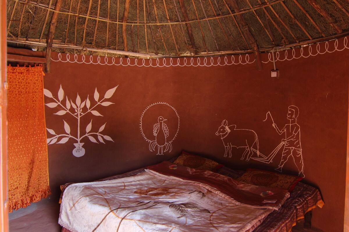 A room with a thatched roof, a bed with patterned bedding, and a wall with a mural.