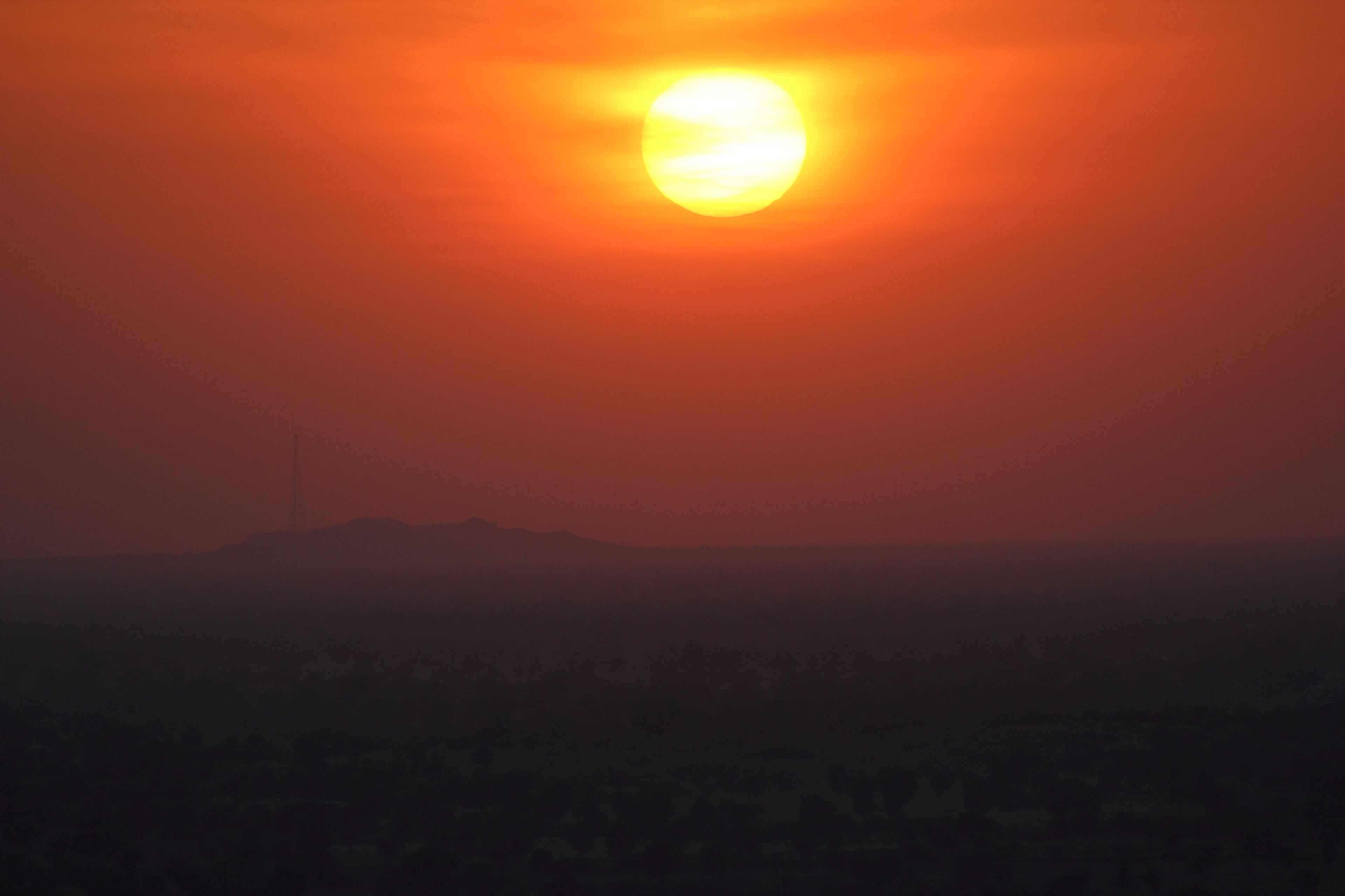Un atardecer sobre un paisaje urbano con una colina destacada en primer plano.
