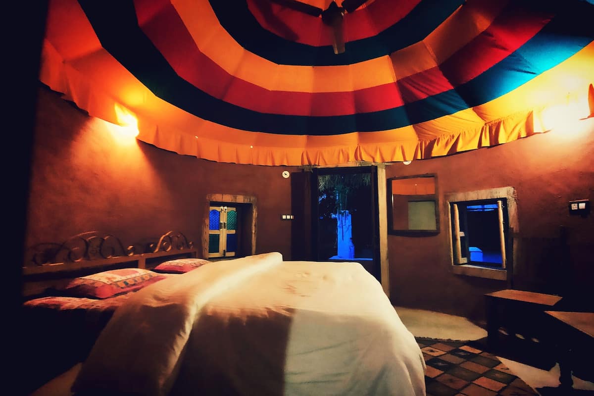 A dimly lit room with a bed, a bench, and two windows with blue lighting.
